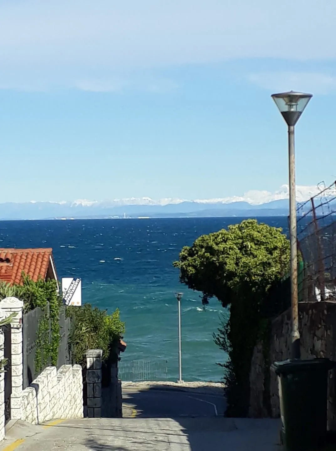 Ulica do morja pri naši hiši, čez zaliv se vidijo zasnežene Alpe